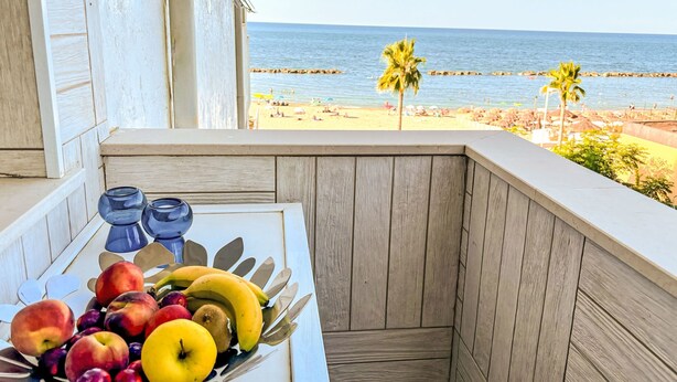 Ein Balkon mit Obstschale, Blick auf den Strand und einer Palme.