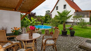 Een terras met rieten meubilair, een zwembad en een huis op de achtergrond.