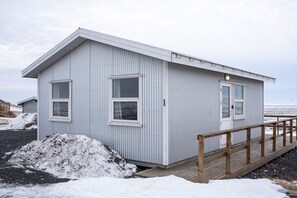 Pieni, yhden kerroksen rakennus, jossa on puinen terassi ja metallinen kaide.