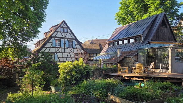 Une maison traditionnelle à colombages, dotée d’une terrasse en bois et d’une véranda en verre.