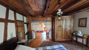 Une chambre traditionnelle en bois, avec un lit, une armoire en bois, une table sur laquelle se trouve une carafe, et une chaise.