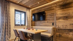 Un comedor moderno con techo de madera, un televisor grande en la pared y una ventana con cortinas.