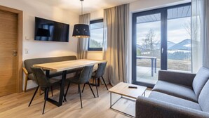 Una sala de estar moderna con una mesa de comedor de madera, un sofá gris y un amplio ventanal con vistas a la montaña.