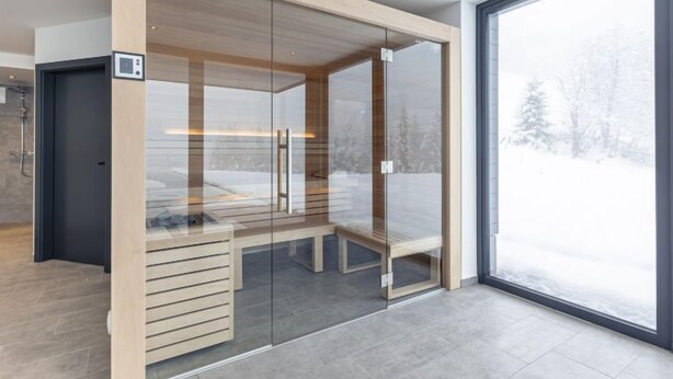 Camera da letto moderna e minimalista con parete divisoria in vetro, una panca in legno e un'ampia finestra con vista su un paesaggio innevato.