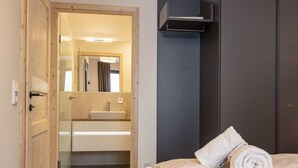 Una camera d'albergo con una porta in legno, un letto con lenzuola bianche, un armadio scuro e un bagno con lavandino e specchio.