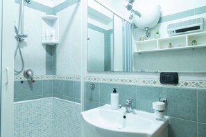 Une salle de bain équipée d’une douche, d’un lavabo, d’un miroir et d’étagères où sont rangés les articles de toilette.