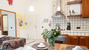 A modern kitchen with a wooden dining table, a vase with flowers, and a tiled backsplash. - Neapolitan Style Apartment (Napoli)