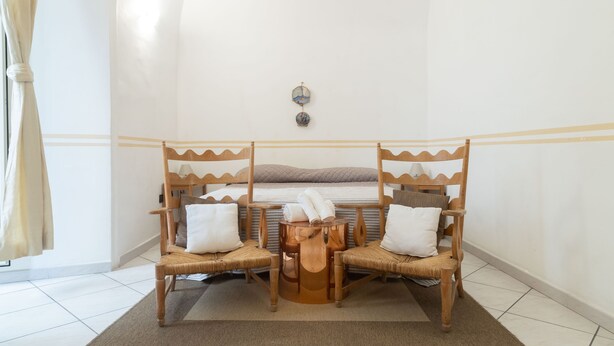 A room with a bed, two wicker chairs, a small round table, and a wall-mounted light fixture. - Neapolitan Style Apartment (Napoli)