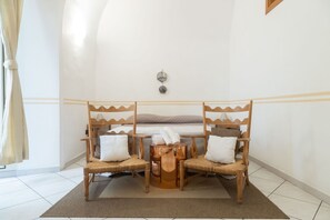 Une pièce comprenant un lit, deux fauteuils en osier, une petite table ronde et un luminaire fixé au mur.