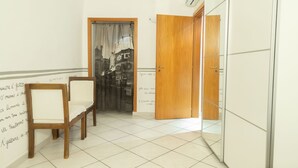 A room with two wooden chairs, a white tiled floor, a wooden door, and a wall with a black and white photograph. - Neapolitan Style Apartment (Napoli)