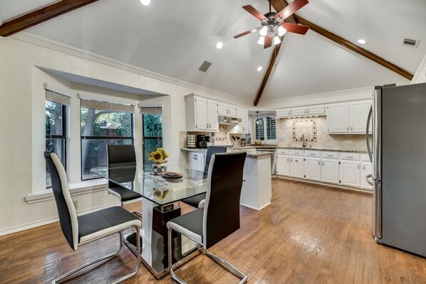 A modern kitchen with white cabinets, a glass dining table, and a ceiling fan.