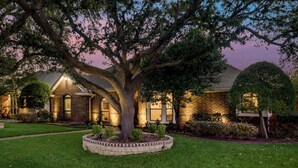 A brick house with a large tree in the front yard, surrounded by well-maintained grass and shrubs. - 4 Bedroom3 Bath,Pool table, Pool, Crib (Plano)