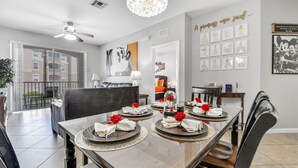 Uma sala de jantar com uma mesa posta para quatro pessoas, um candelabro e uma parede com quadros.
