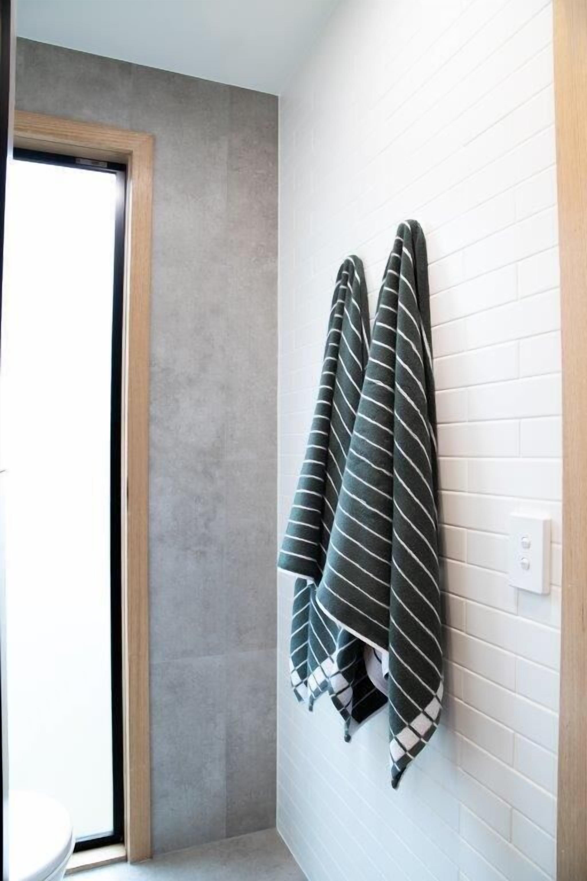 A bathroom with a white tiled wall, a wooden door, and two striped towels hanging on the wall.
