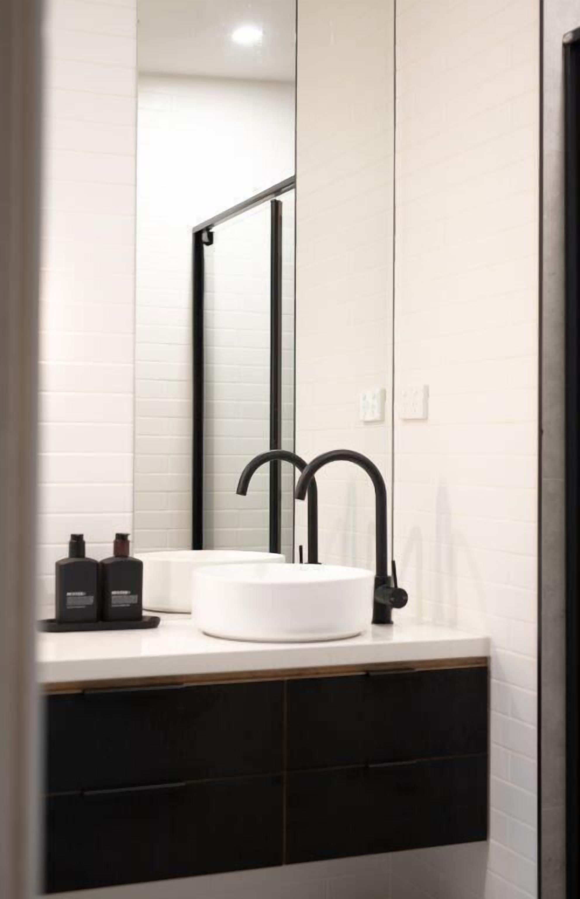 Ein modernes Badezimmer mit einem weißen Waschbecken, einem schwarzen Wasserhahn und einem großen Spiegel.