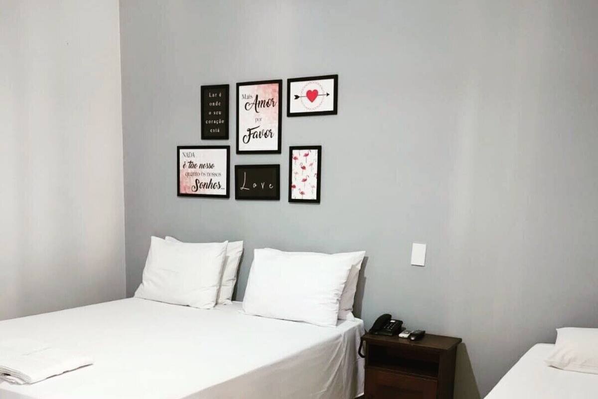 Une chambre d’hôtel avec un lit, une table de chevet, un téléphone et un mur orné de citations inspirantes encadrées.