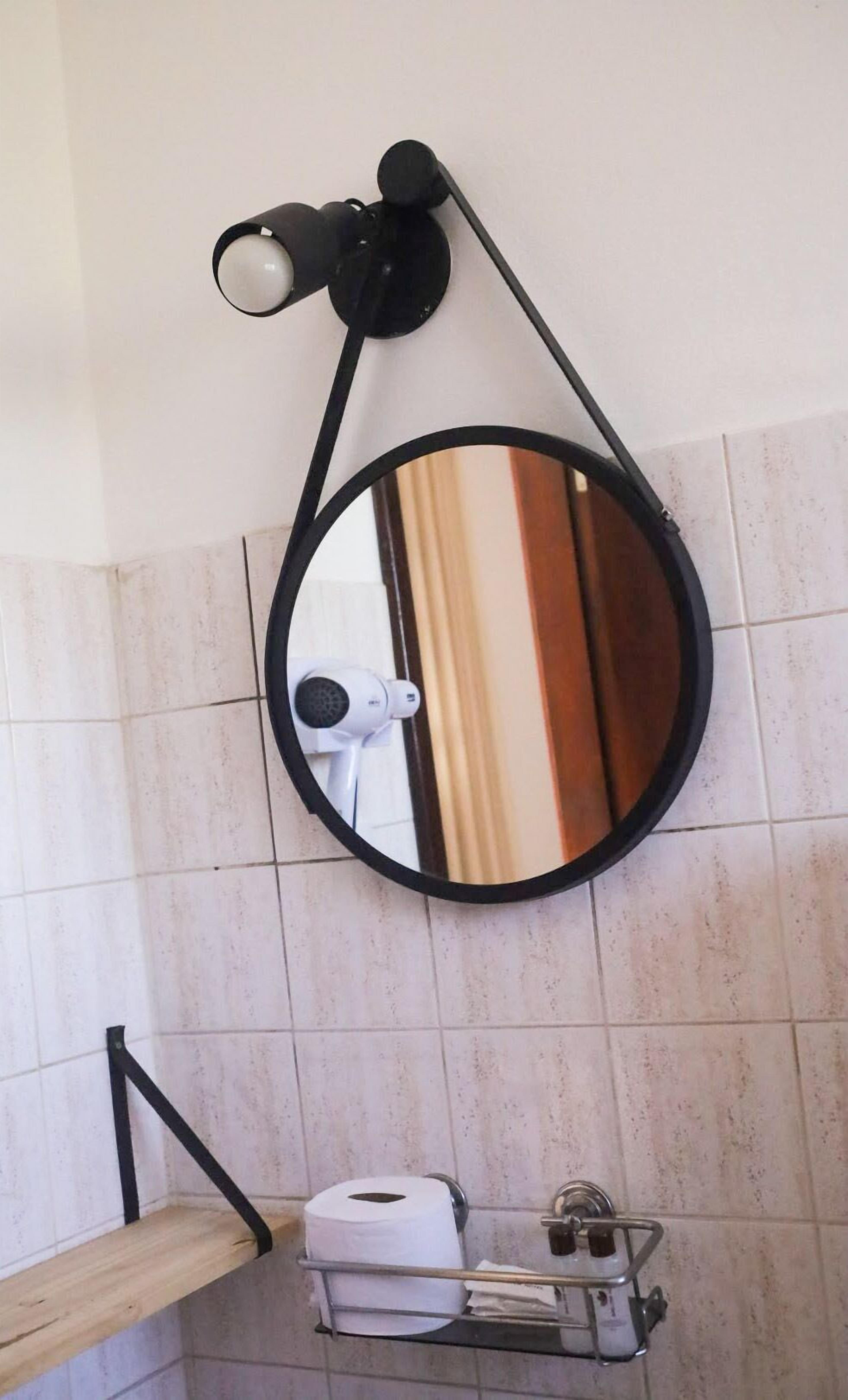 Ein Badezimmer mit rundem Spiegel, Fön und Toilettenpapierhalterung.