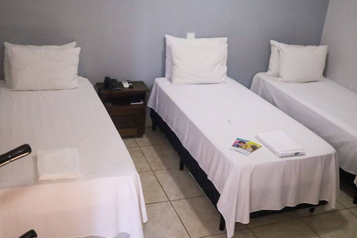 Une chambre d’hôtel avec trois lits simples, une table de chevet avec un téléphone et un magazine sur le lit.