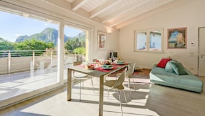 A spacious room with a dining table set for four, a sofa, and a balcony with a mountain view. - Mirabelle - Apartment With Terrace & Views (Dro)