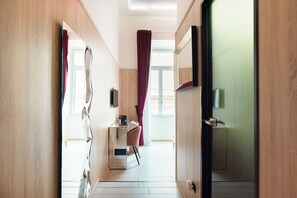 A hotel room with a wooden floor, a desk with a chair, a bed, and a window with curtains. - Kore Luxury Suite & Spa  (Naples)