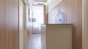 Corredor de hotel com paredes de madeira, um balcão de recepção e uma porta com sinal de número.