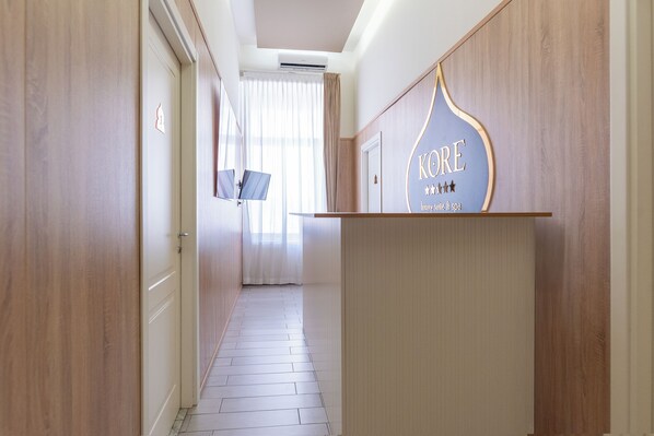 A hotel corridor with wooden walls, a reception desk, and a door with a number sign. - Kore Luxury Suite & Spa  (Naples)