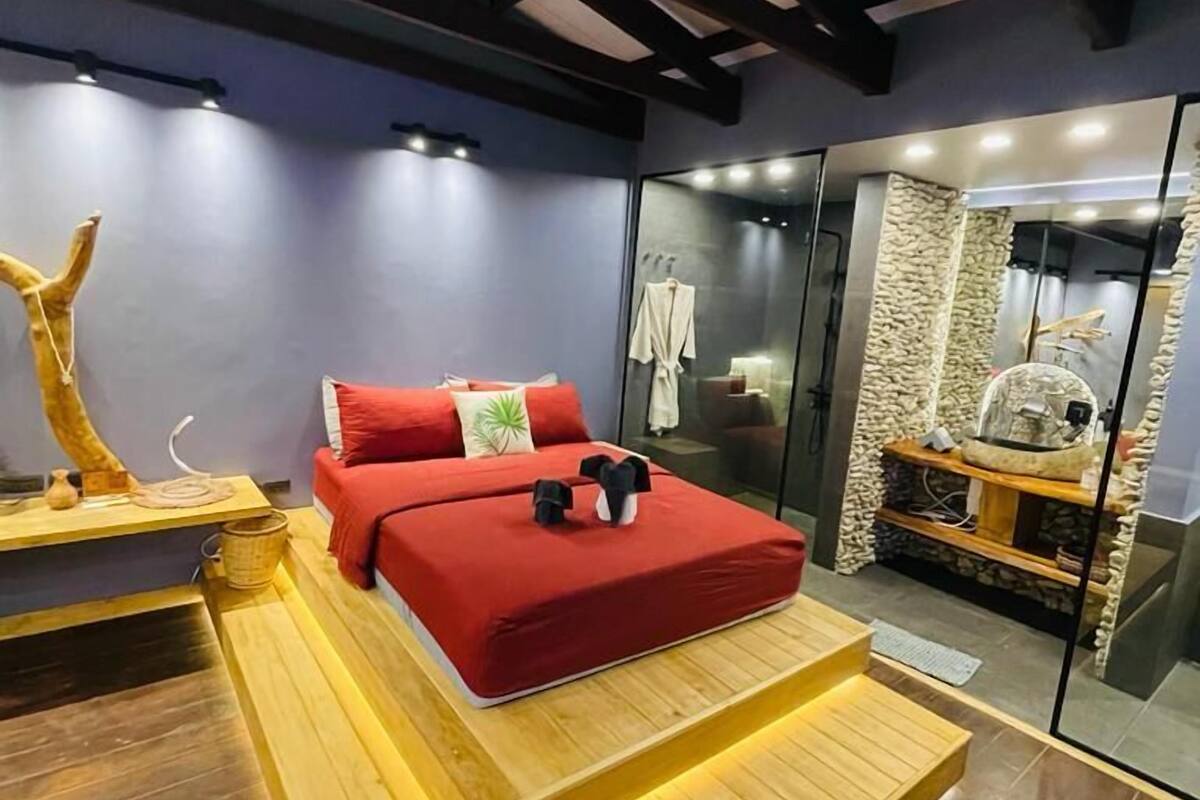 A modern bedroom with a wooden platform bed, a red mattress, and a glass shower enclosure.
