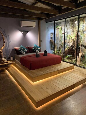 Un dormitorio moderno con una cama empotrada, un pequeño rincón de descanso y un amplio ventanal con vistas a un jardín interior natural.