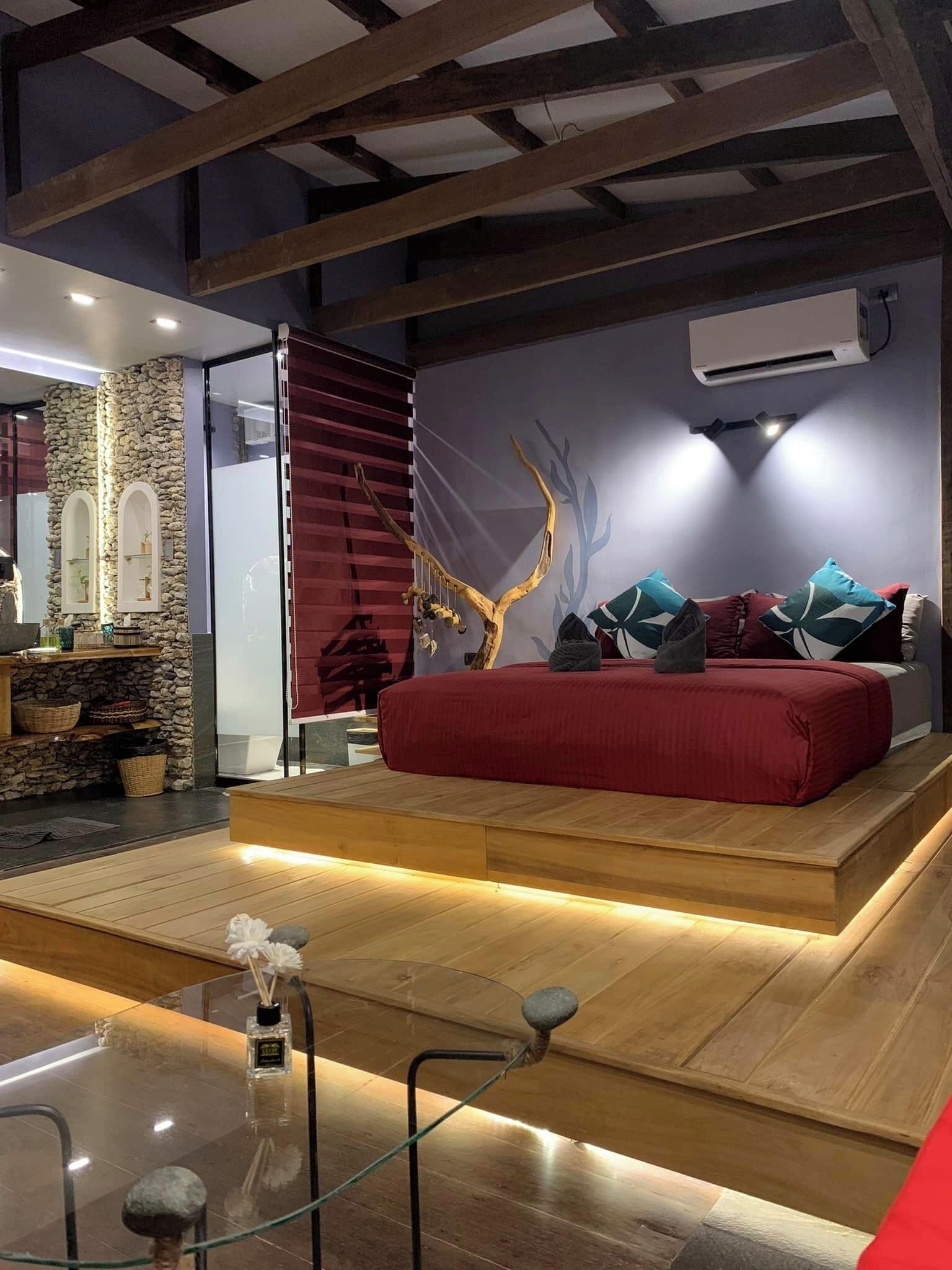 Un dormitorio moderno con una cama roja, una pared de piedra y un techo de madera.