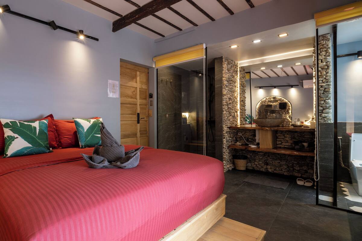 A bedroom with a bed, a wooden wardrobe, a bathroom with a stone wall, and a shower area.
