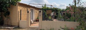 Un bâtiment rustique doté d’une porte, d’un petit porche et d’un jardin agrémenté de plantes et de fleurs.