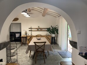 Un espace repas avec une longue table, des chaises et une cuisine en arrière-plan.