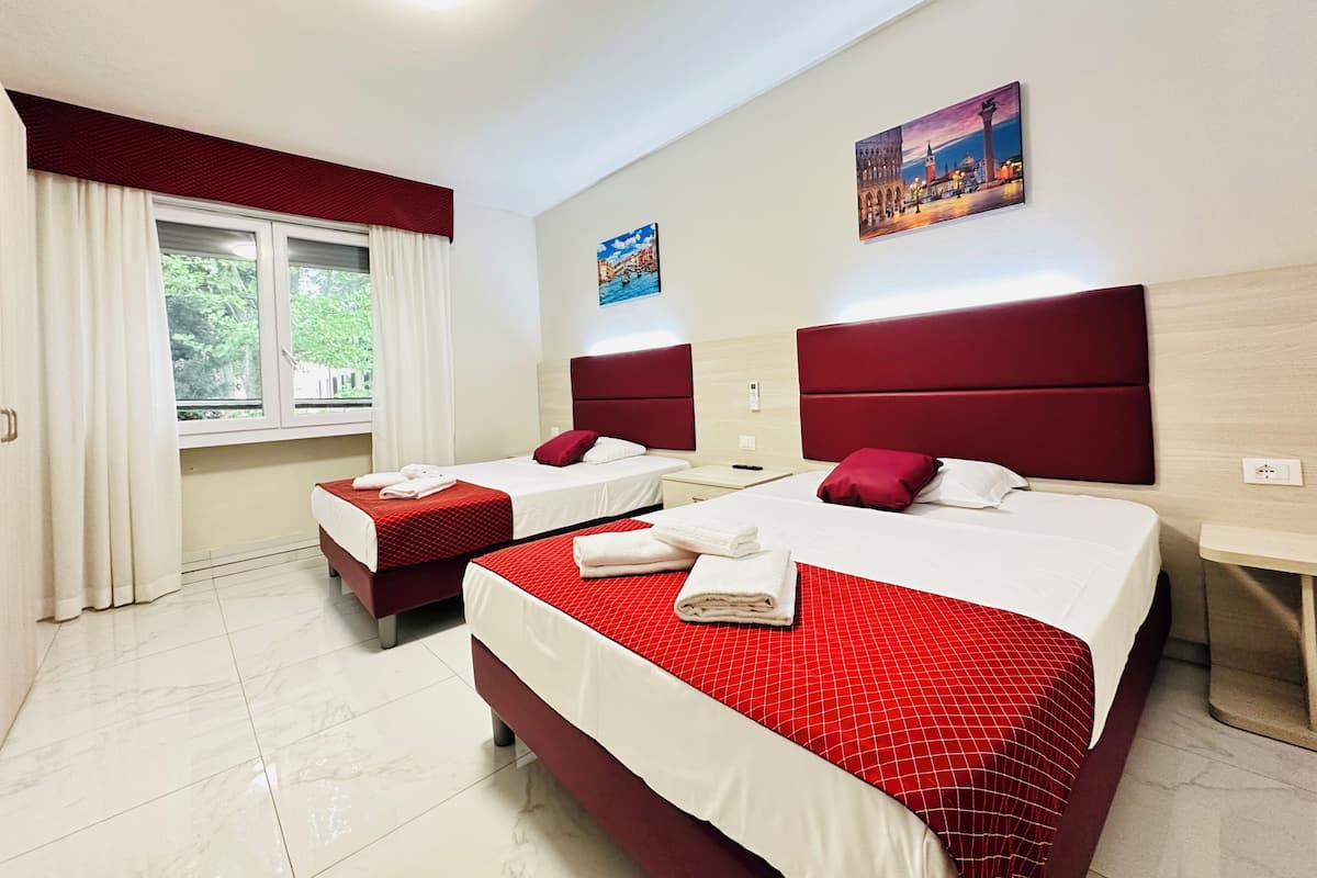 A hotel room with two beds, red bedding, a window with curtains, and artwork on the walls.