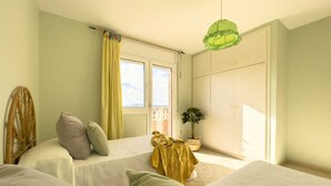 Ein Schlafzimmer mit zwei Betten, einem mit Vorhängen versehenen Fenster, einer hängenden grünen Lampe und einem Blumentopf.