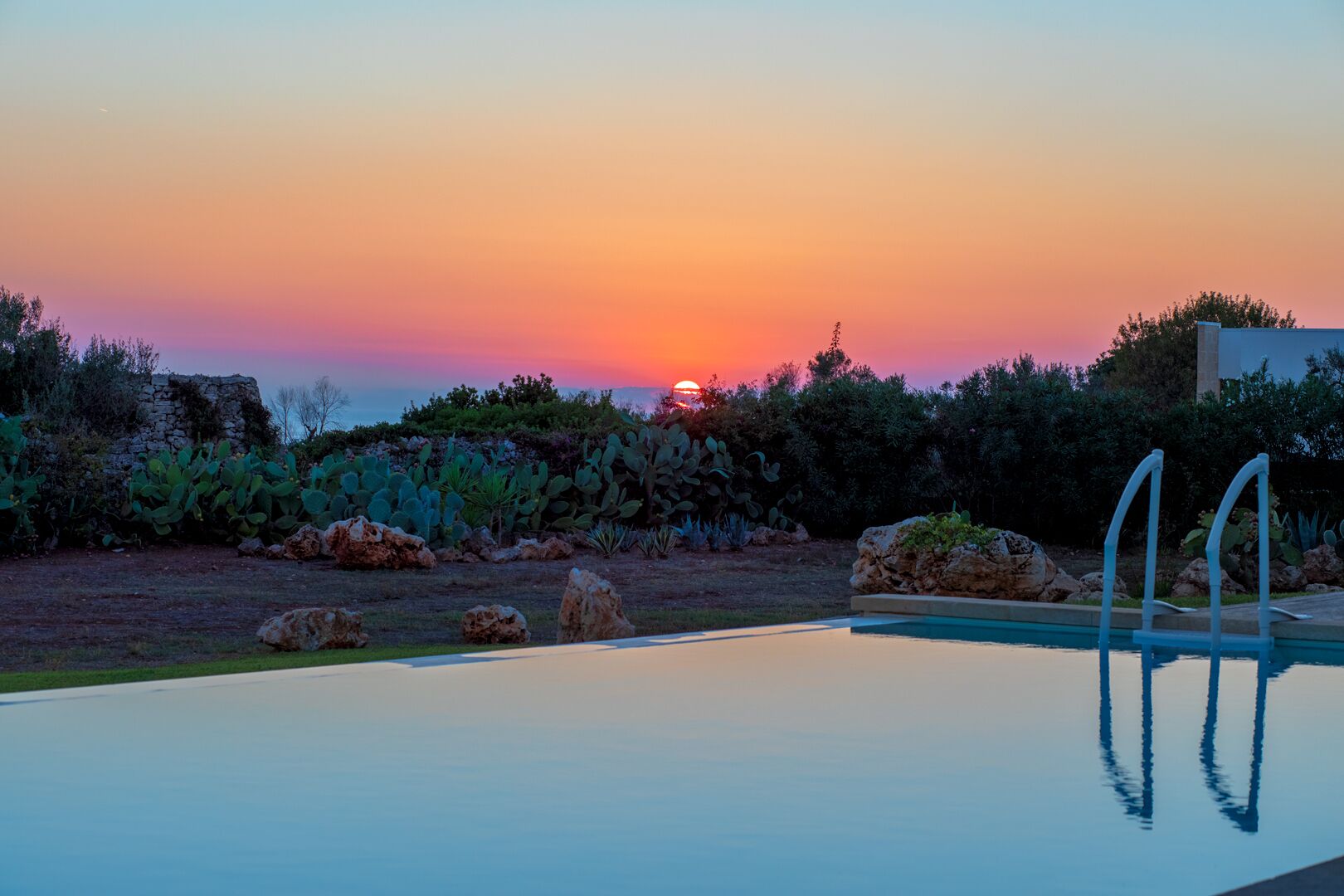 Ein Pool mit Blick auf einen Sonnenuntergang, umgeben von Felsen und Kakteen.