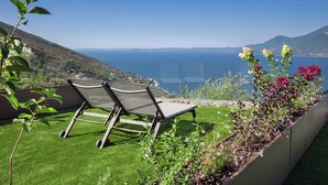 En terrass med två solstolar med utsikt över ett vackert landskap med hav och kullar.
