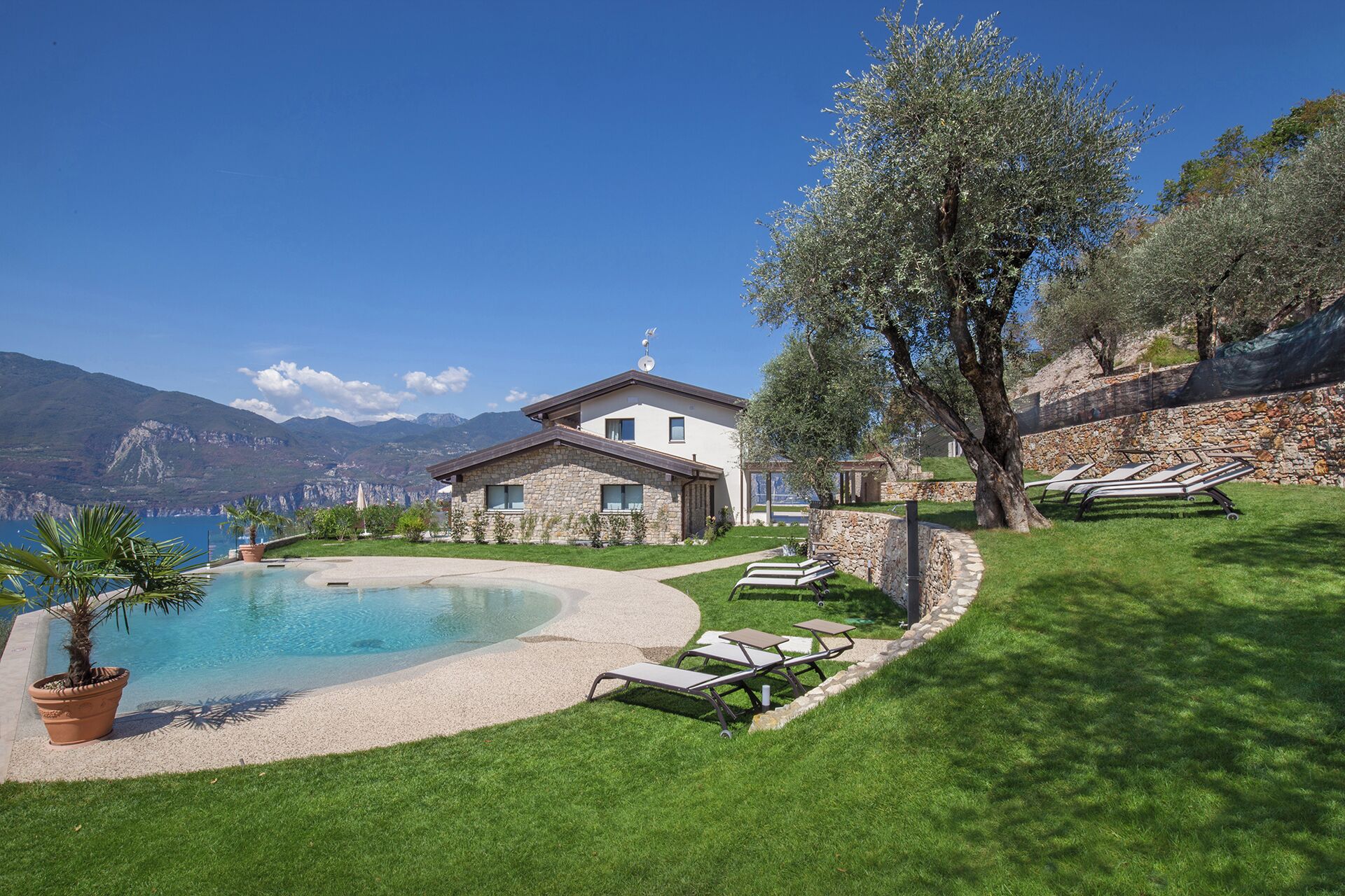 A house with a swimming pool, a stone wall, and a view of mountains.