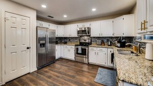 A modern kitchen with white cabinets, stainless steel appliances, and a granite countertop. - Updated 4 Bedroom Home Pool, Sleeps 8 Wifi Garage (Carrollton)