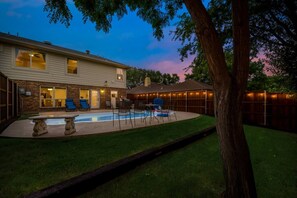 A backyard with a swimming pool, a covered patio, and a house.