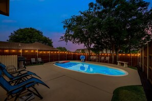 Un giardino sul retro con piscina, sedie a sdraio e luci decorative.