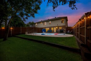 A two-story house with a backyard pool, a wooden fence, and outdoor furniture.