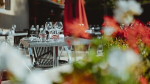 Een buiten eethoek met tafels voor twee personen, met helder glaswerk en een rode parasol.