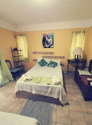 A hotel room with a bed, a desk, a chair, a shelf, and a picture on the wall.