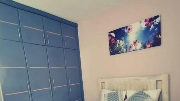 Makuuhuoneessa on sänky, sininen vaatekaappi ja seinällä kukkakuvioitu taulu.