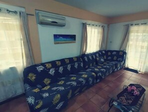 A living room with a sofa, air conditioning unit, and a painting on the wall.