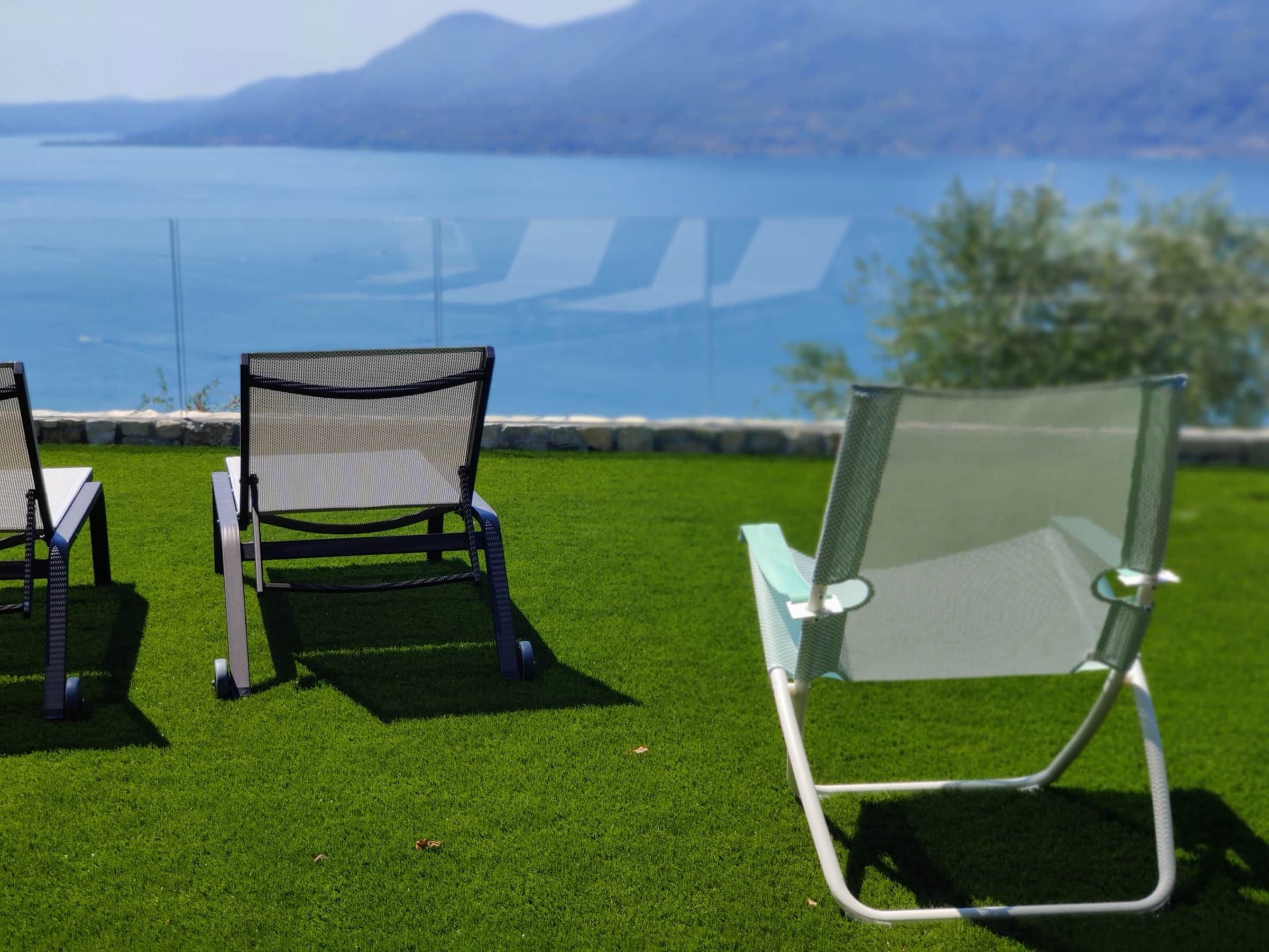 Twee buitenstoelen op kunstgras met uitzicht op een wateroppervlak en bergen op de achtergrond.