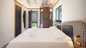 A modern hotel room with a large bed, a wardrobe, a seating area with patterned cushions, and a view of a stone wall and greenery outside. - Villa Divina22-APT Unica-With pool and lake view (Veneto)