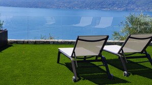 Two lounge chairs on a grassy lawn with a view of a lake and mountains in the background. - Villa Divina22-APT Unica-With pool and lake view (Veneto)
