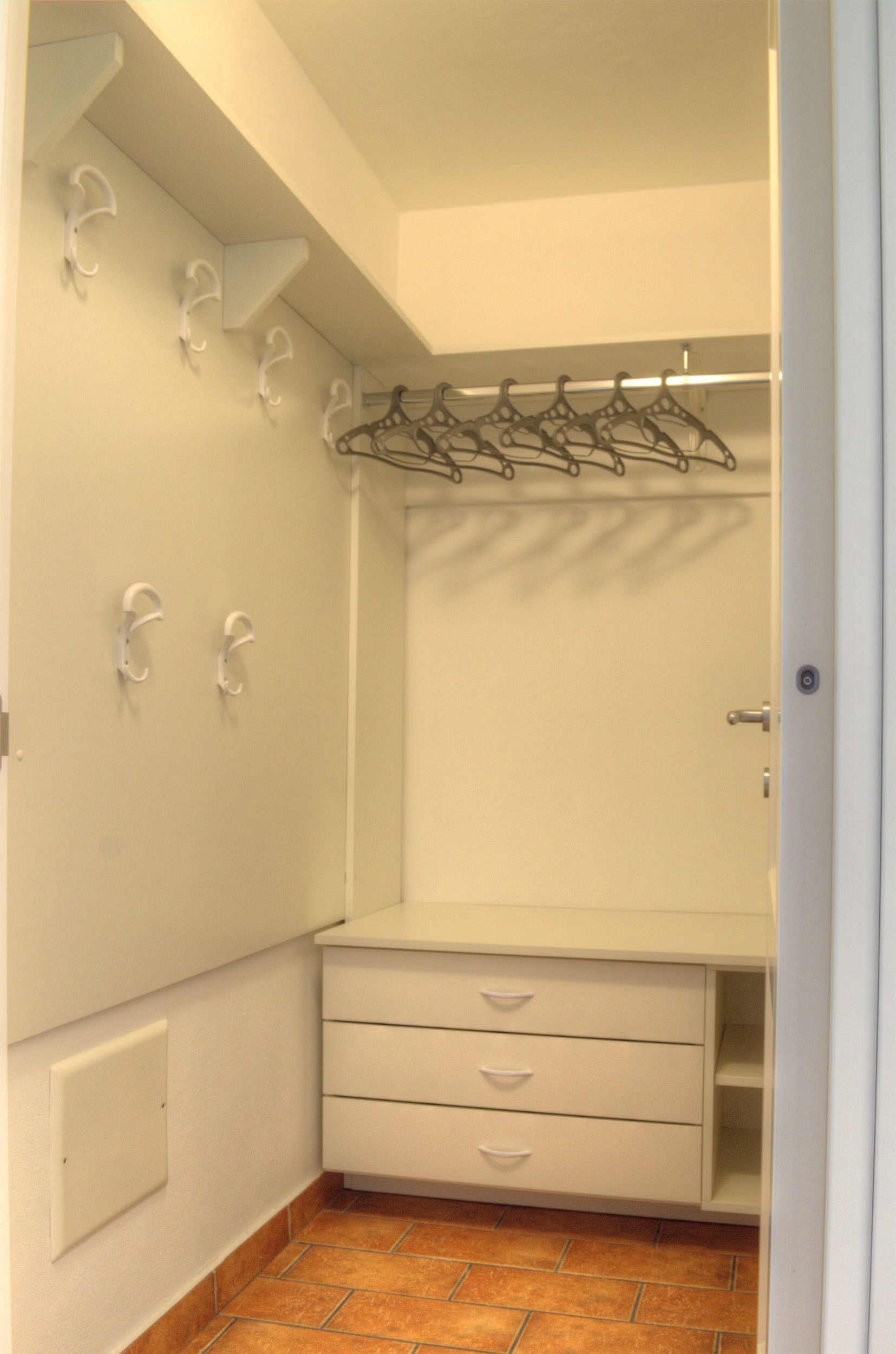 Un dressing avec des murs blancs, un sol carrelé et un porte-manteau en métal.