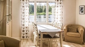 En matplats med ett bord dukat för fyra personer, omgiven av stolar, en soffa och ett fönster med utsikt över en sjö.